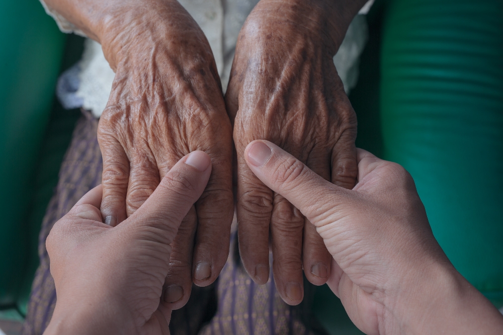 Caregiver holds elderly woman's hands, thumbs gently supporting.